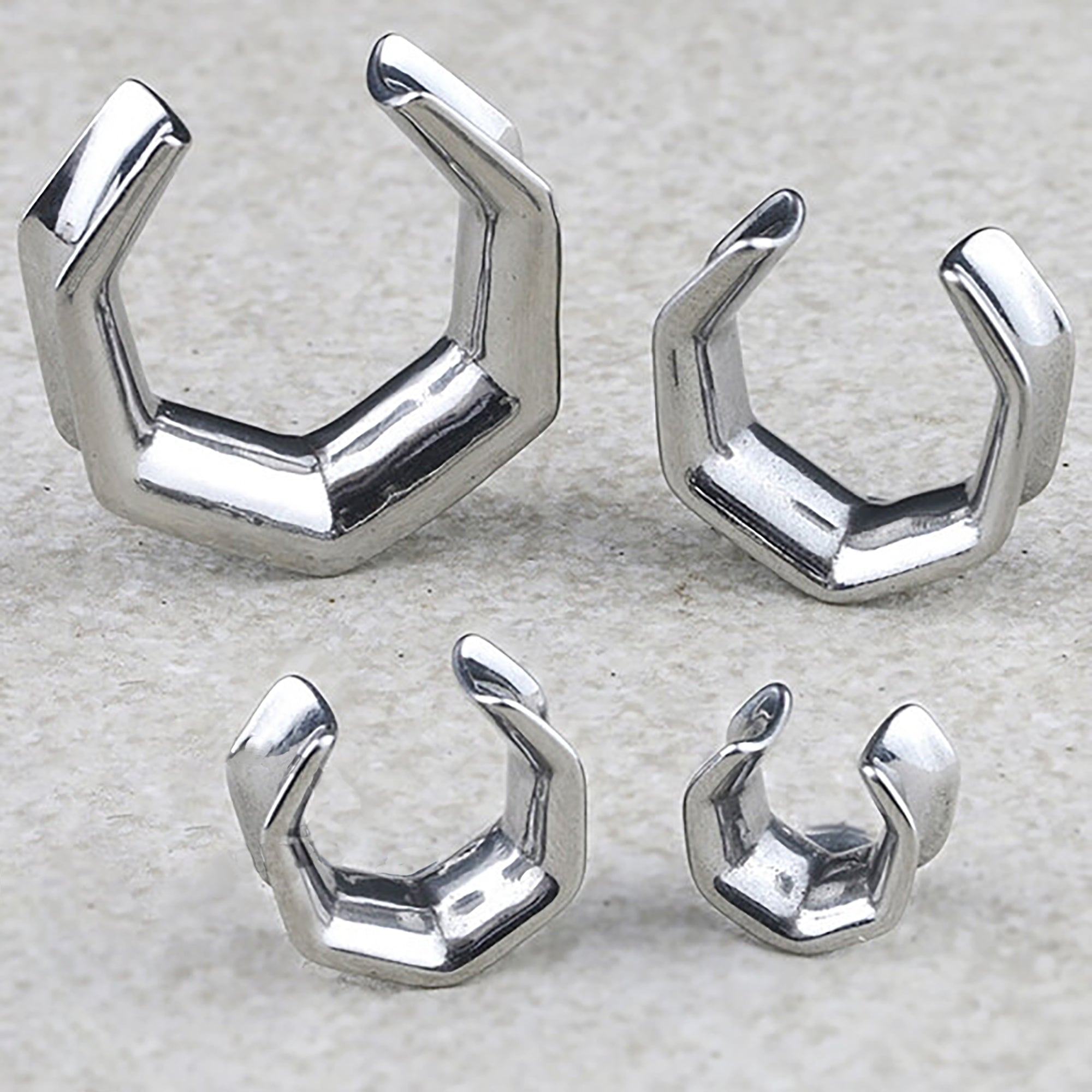 A close-up image showcases four OCTAGON Minimalist Saddle Tunnels in Silver by Kaya Movement, arranged on a light surface. The plugs, ranging from 6mm to 25mm (2g to 1 Inch), include two larger ones positioned at the back and two smaller ones in front.
